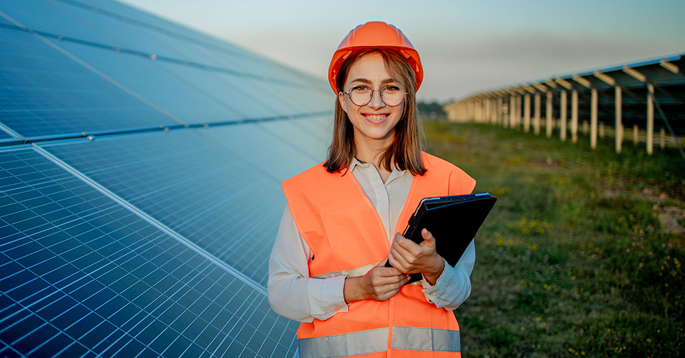 A young woman wearing PPE in the middle of a solar power array.