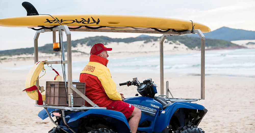 A surf-lifesaver sits in a 4WD buggy watching out over the surf break.