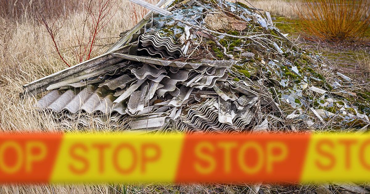 Pile of dumped asbestos-containing building materials behind hazard tape in a grassy area, illustrating the risks of illegal asbestos disposal.