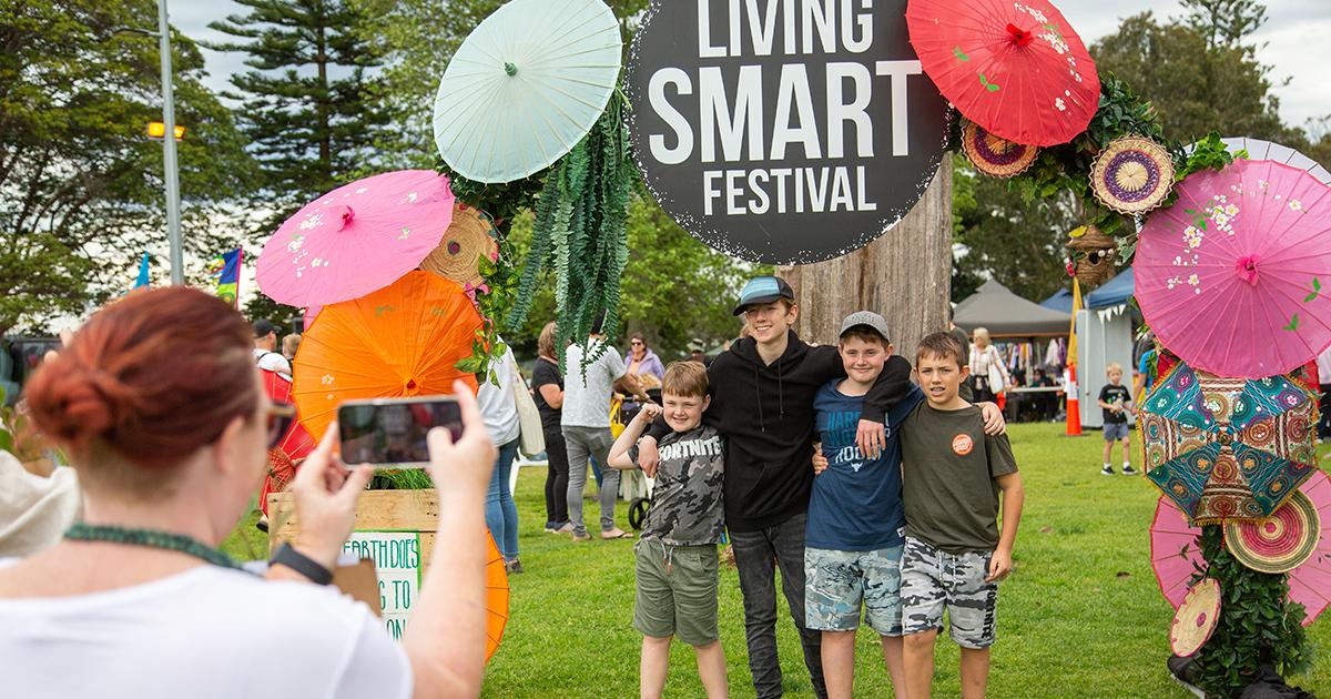 Children pose for a photo beneath a colourful display of umbrellas at the Living Smart Festival, while a visitor takes their picture.