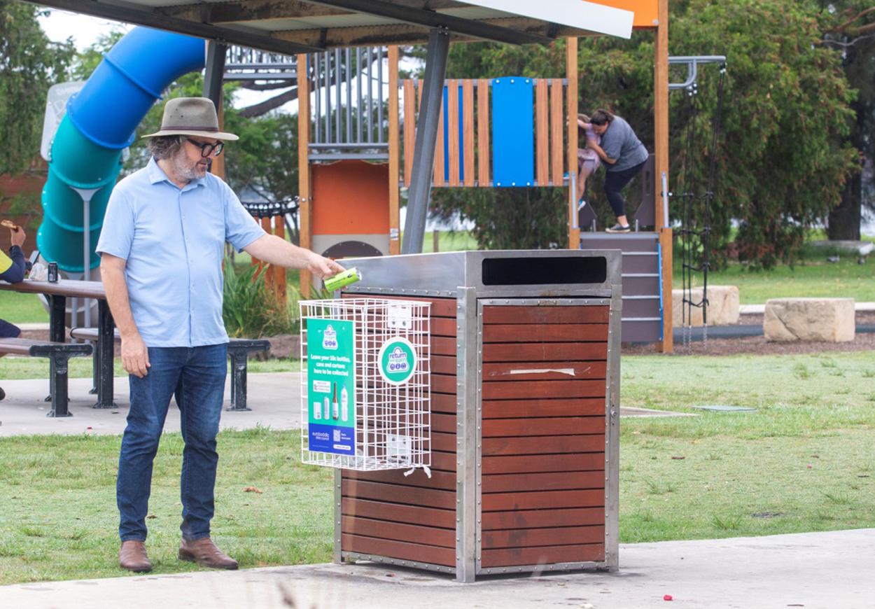 Person using a park bin with a container recycling cage.
