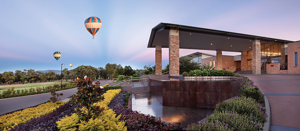 Image shows entrance to Crowne Plaza Hunter Valley with hot air balloons in the background.