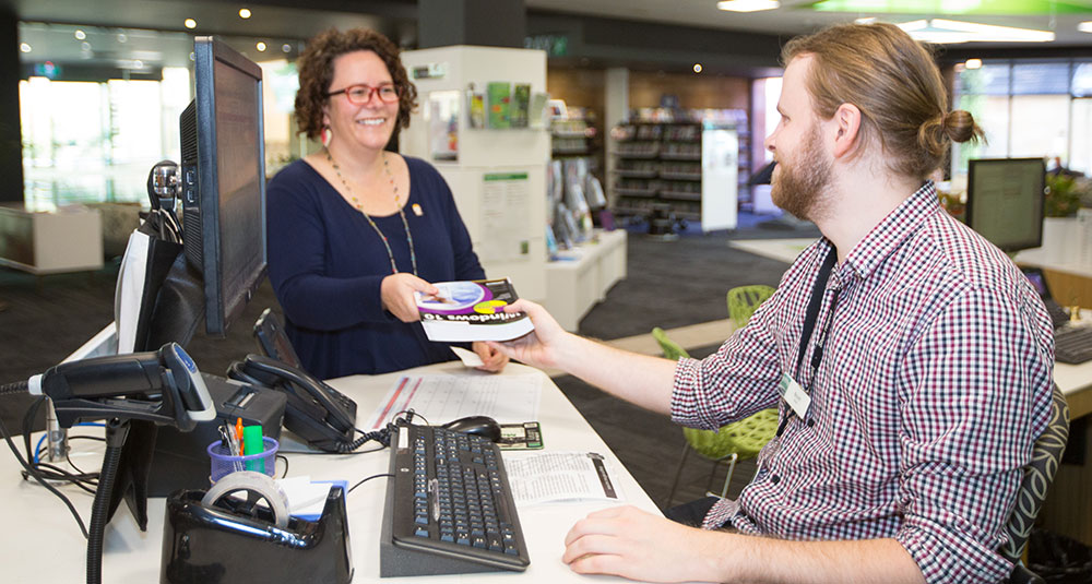 A library patron returns a book to a staff member at a council library.