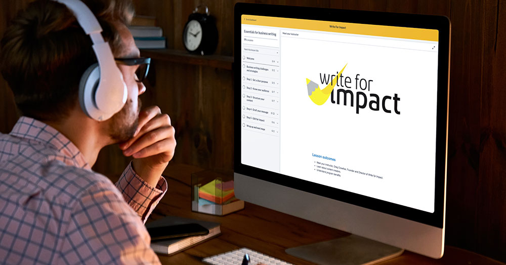 A man weraing headphones sits in front of an iMac that has Write for Impact logo on the screen.