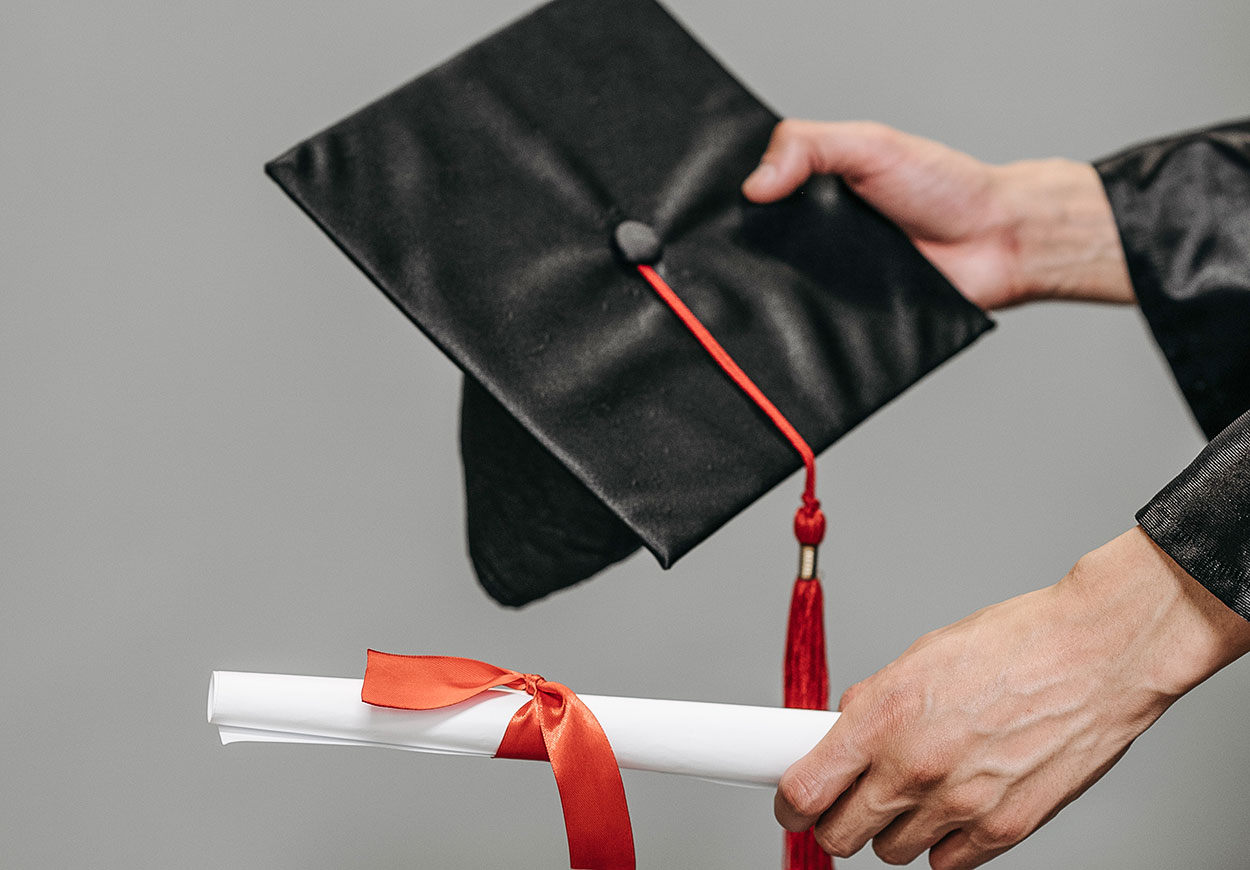 A person (obscured) holding a graduation cap and rolled certificate.