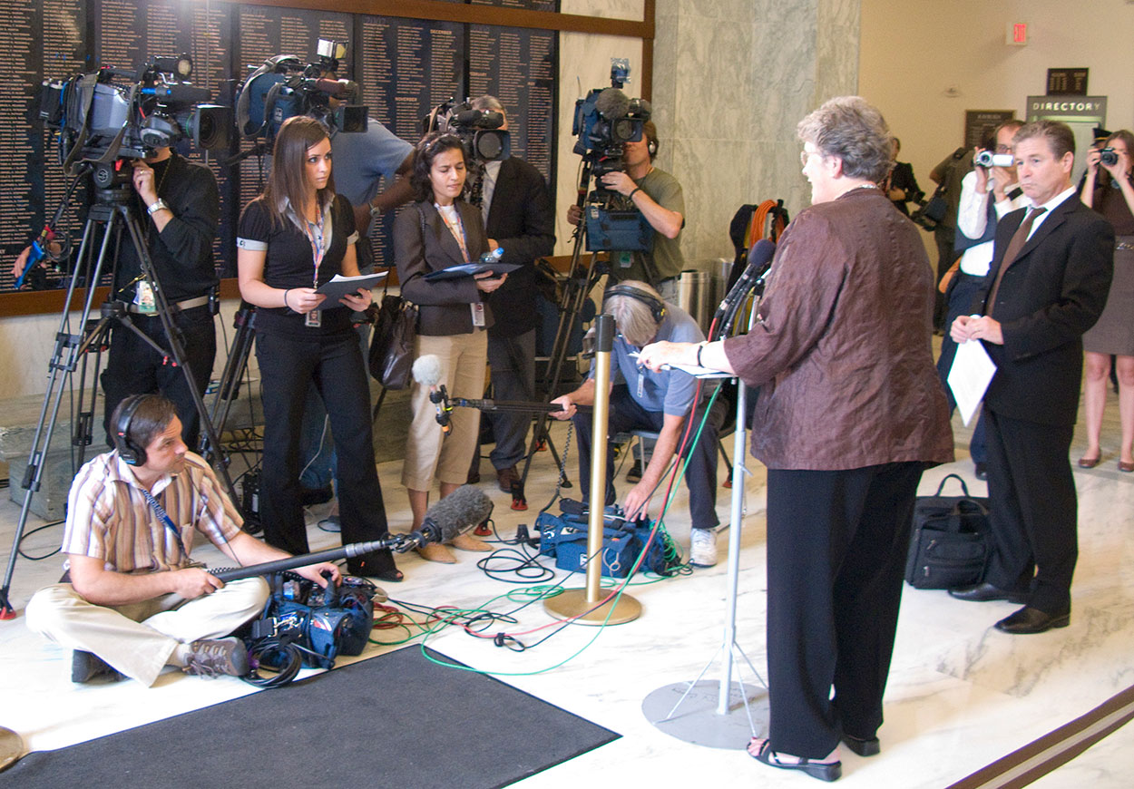 A woman fronts journalists and TV cameras.