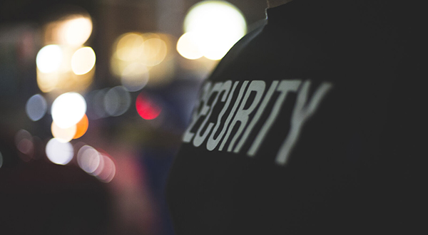 A man (from shoulders down) wearing a black T-shirt with the word security .
