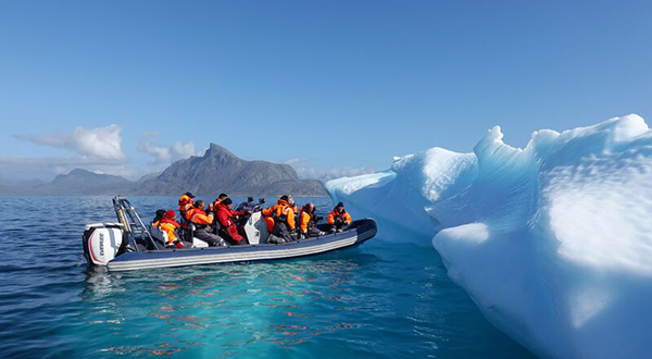 An inflatable boat full of what are apparently scientists pull up against a melting iceberg.