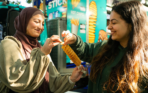 Two women share a fried potato twirl at Bankstown Bites festival.