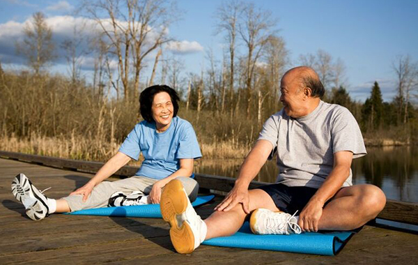 An older couple sitting and stretching on yoga mats.